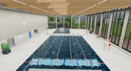 Rendered indoor swimming pool seen from the diving board, with lane ropes, a lifeguard chair and a glass facade
